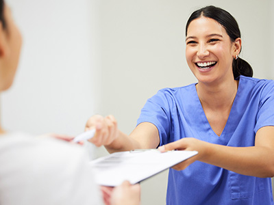 A smiling female nurse handing over papers with a patient sitting across from her.