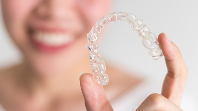 A person holding a clear plastic tray containing multiple transparent retainers.