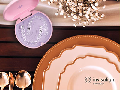 The image displays a collection of tableware items including plates, bowls, and a cosmetic compact with a purple lid, arranged on a wooden surface with a white cloth underneath, set against a background that includes a pink toothbrush holder and a framed picture of a smiling face.