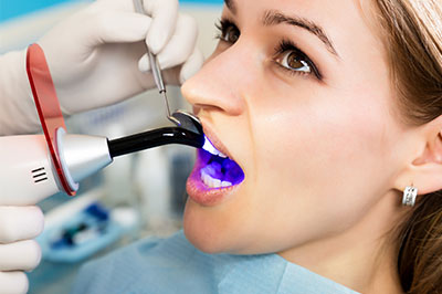 A woman undergoing dental treatment with a device that appears to be scanning her teeth, surrounded by medical professionals in a dental office setting.