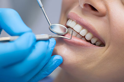 The image shows a dental professional performing a teeth cleaning procedure on a patient, with both hands focused on the task using specialized tools while wearing gloves for hygiene.