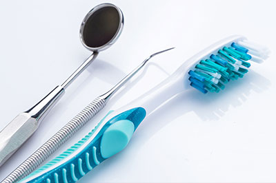 The image features dental tools including a toothbrush with blue bristles, a pair of scissors, and a set of dental instruments on a white background.