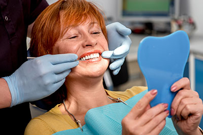 A woman receiving dental care with a smile, holding a blue dental model, while seated on a dental chair.