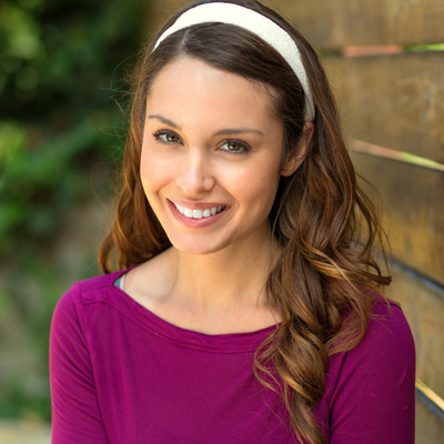 The image shows a woman with long hair smiling at the camera, wearing a purple top and a headband.