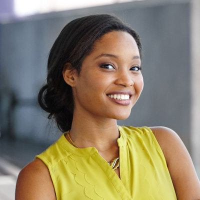 A young woman with a radiant smile, wearing a yellow top and posing confidently against a backdrop.