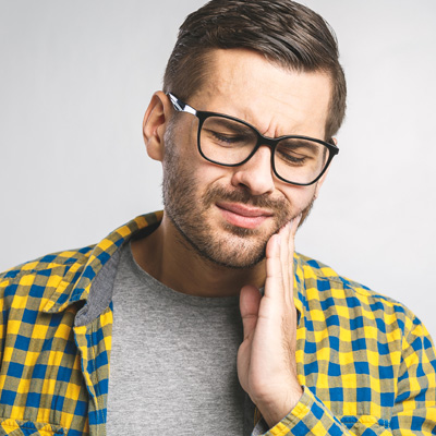A man with glasses and a beard, wearing a yellow plaid shirt, expressing concern or discomfort with his hand on his chin while looking upwards.