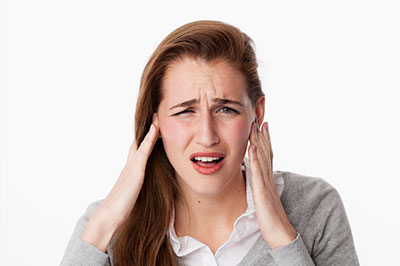 A woman with her hand on her head, likely expressing discomfort or pain, against a white background.