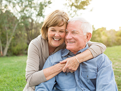 An elderly couple embracing each other outdoors during daylight.