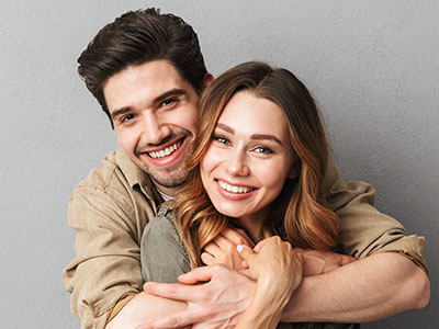 A man and woman are embracing each other with smiles, posing for a portrait against a neutral background.