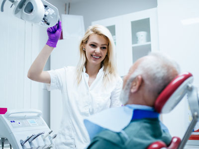 A dental professional is assisting an elderly patient with dental equipment in a clinic setting.