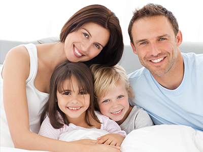 The image depicts a family of four adults and three children posing together on a bed with a happy expression.