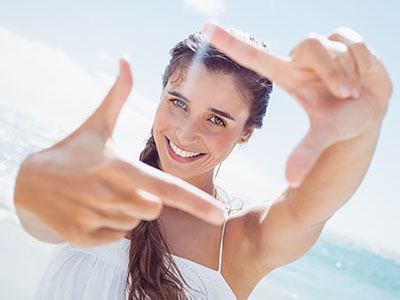 A woman posing with her finger pointing at the camera against a beach backdrop.